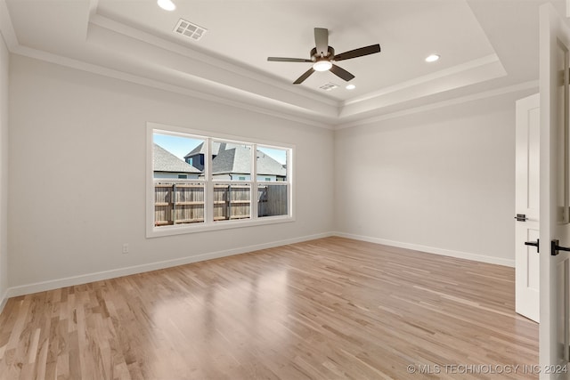 empty room with ornamental molding, light wood-type flooring, ceiling fan, and a raised ceiling