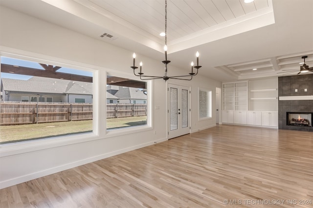 unfurnished living room with light hardwood / wood-style floors, crown molding, built in features, a tray ceiling, and a tile fireplace