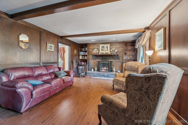 living room featuring beam ceiling, hardwood / wood-style flooring, a brick fireplace, wood walls, and built in features