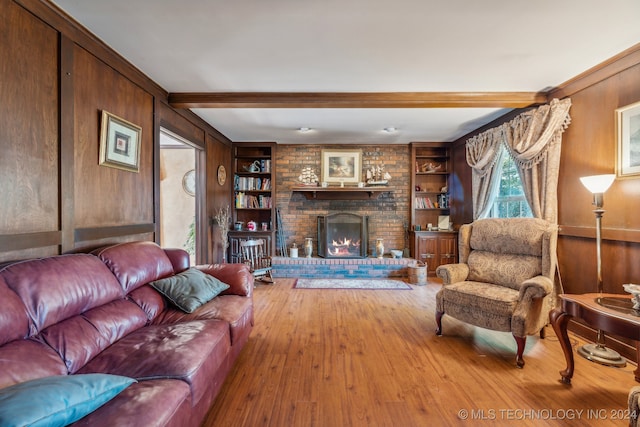 living room with beamed ceiling, wooden walls, wood-type flooring, a brick fireplace, and built in features