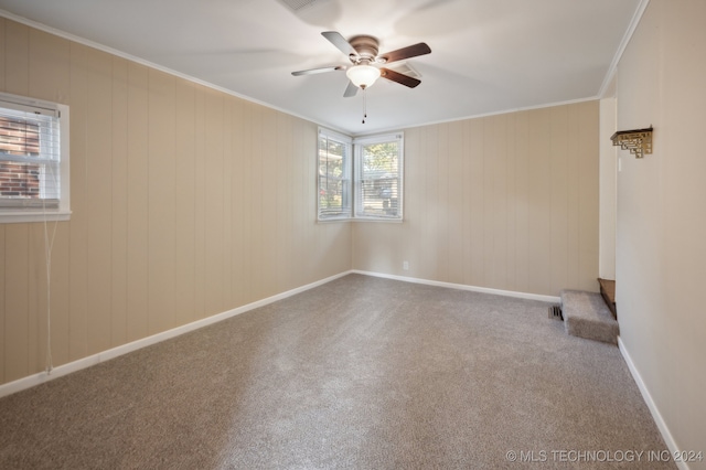 carpeted spare room featuring ceiling fan, wood walls, and ornamental molding