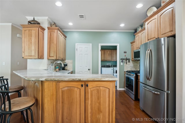 kitchen featuring a breakfast bar, sink, washing machine and dryer, kitchen peninsula, and stainless steel appliances