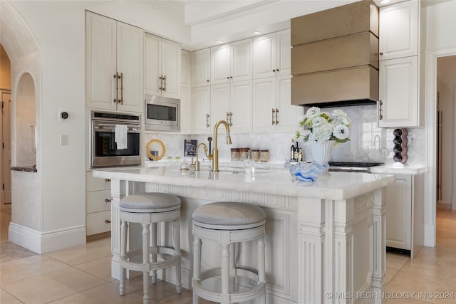 kitchen featuring an island with sink, stainless steel appliances, a breakfast bar, light tile patterned flooring, and white cabinets