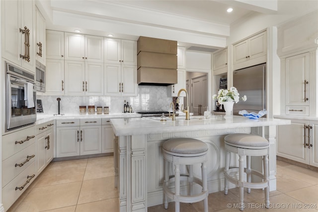 kitchen featuring custom exhaust hood, white cabinetry, a kitchen island with sink, and built in appliances