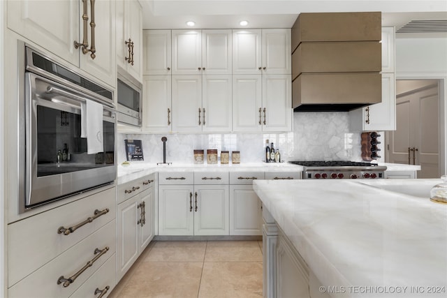 kitchen with backsplash, white cabinetry, stainless steel appliances, light tile patterned floors, and premium range hood