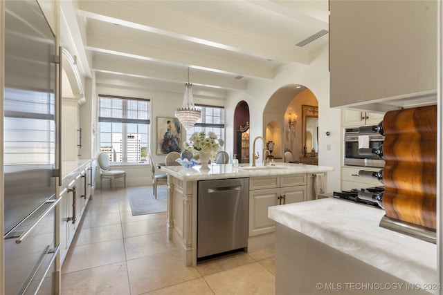 kitchen featuring beam ceiling, an island with sink, appliances with stainless steel finishes, sink, and decorative light fixtures