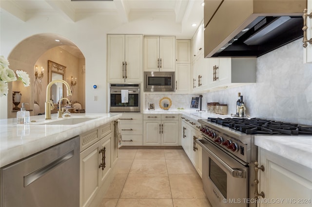 kitchen featuring wall chimney range hood, appliances with stainless steel finishes, sink, beam ceiling, and light tile patterned floors