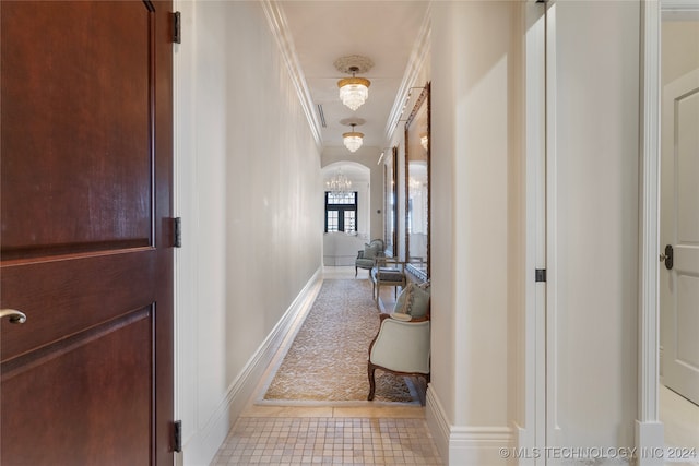 hallway with crown molding, an inviting chandelier, and light tile patterned floors