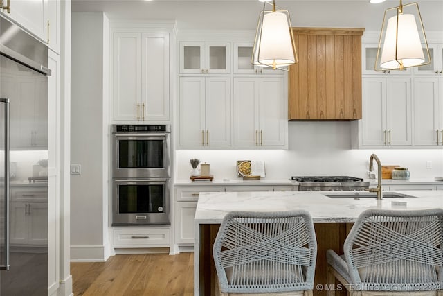 kitchen with stainless steel double oven, light hardwood / wood-style flooring, pendant lighting, white cabinetry, and light stone counters