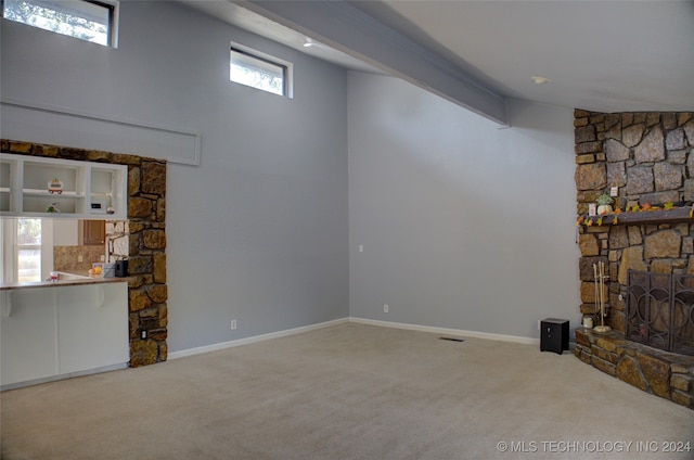 unfurnished living room featuring carpet flooring, a wealth of natural light, and a stone fireplace