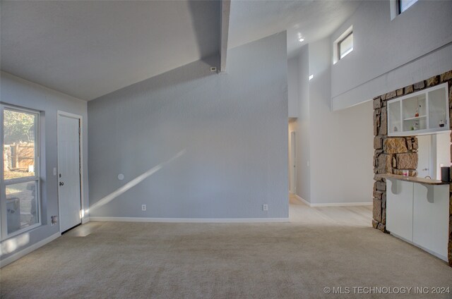 unfurnished living room featuring light carpet and high vaulted ceiling