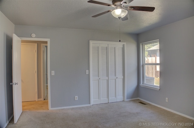 unfurnished bedroom featuring ceiling fan, a textured ceiling, a closet, and light carpet