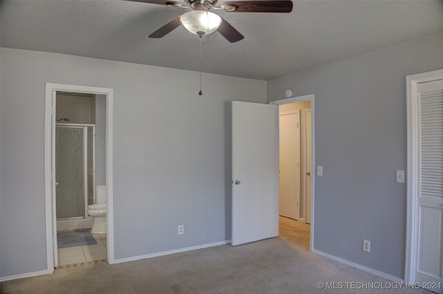 unfurnished bedroom featuring ceiling fan, light colored carpet, a textured ceiling, and ensuite bathroom