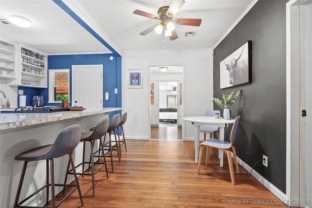 kitchen with ceiling fan, light stone counters, light wood-type flooring, crown molding, and a kitchen bar