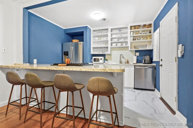 kitchen featuring stainless steel appliances, wood-type flooring, crown molding, and a kitchen bar