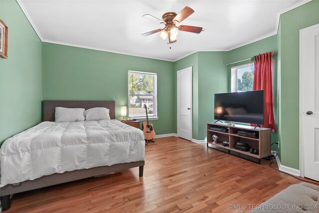 bedroom featuring ceiling fan, hardwood / wood-style flooring, ornamental molding, and multiple windows