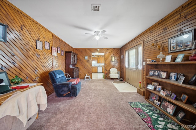 sitting room with wooden walls, carpet flooring, and ceiling fan