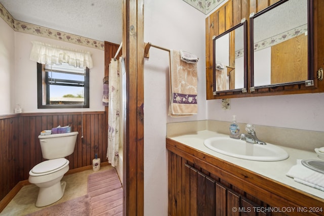 bathroom with vanity, wooden walls, a textured ceiling, and toilet