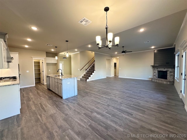 kitchen with dark hardwood / wood-style floors, a fireplace, white cabinets, hanging light fixtures, and a center island with sink