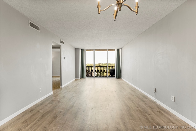 unfurnished room featuring a textured ceiling, a wall of windows, a notable chandelier, and light hardwood / wood-style flooring