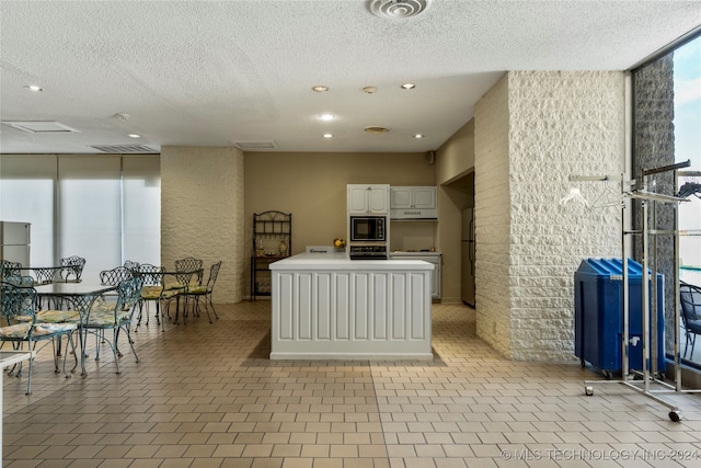 kitchen with a wall of windows, black microwave, a textured ceiling, and white cabinetry