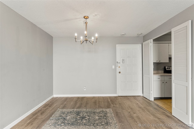 unfurnished dining area featuring an inviting chandelier, a textured ceiling, and light wood-type flooring