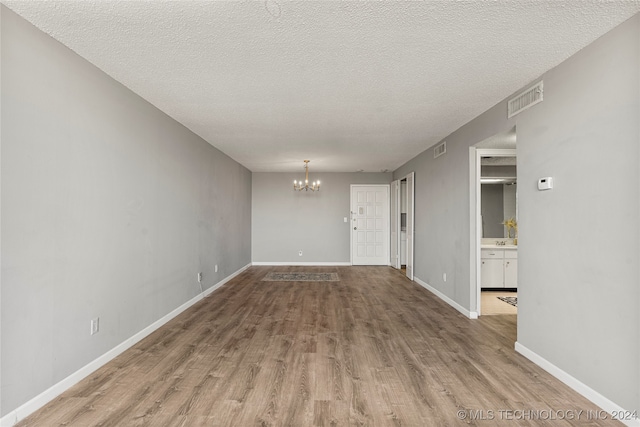 unfurnished room with a notable chandelier, wood-type flooring, and a textured ceiling