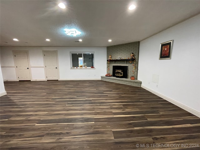 unfurnished living room featuring a textured ceiling, a brick fireplace, and dark hardwood / wood-style floors