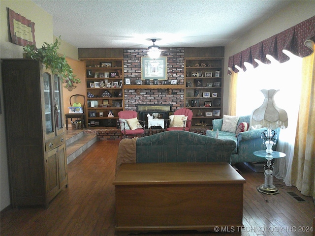 living room featuring ceiling fan, a brick fireplace, dark hardwood / wood-style floors, and a textured ceiling