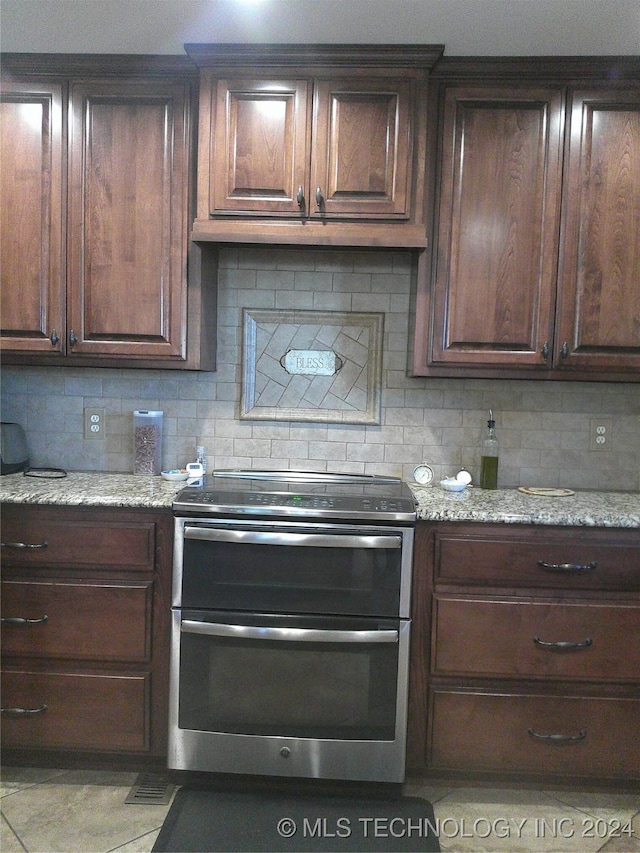 kitchen featuring double oven range, backsplash, dark brown cabinets, and light stone countertops