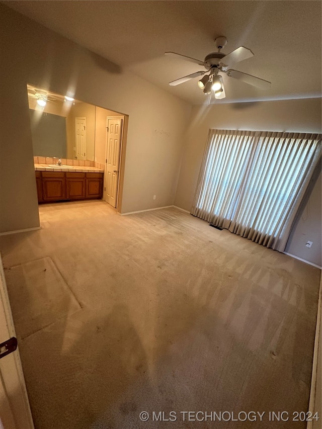 unfurnished bedroom with light carpet, ensuite bathroom, and ceiling fan