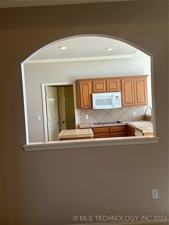 kitchen featuring tile counters, stovetop, decorative backsplash, and sink