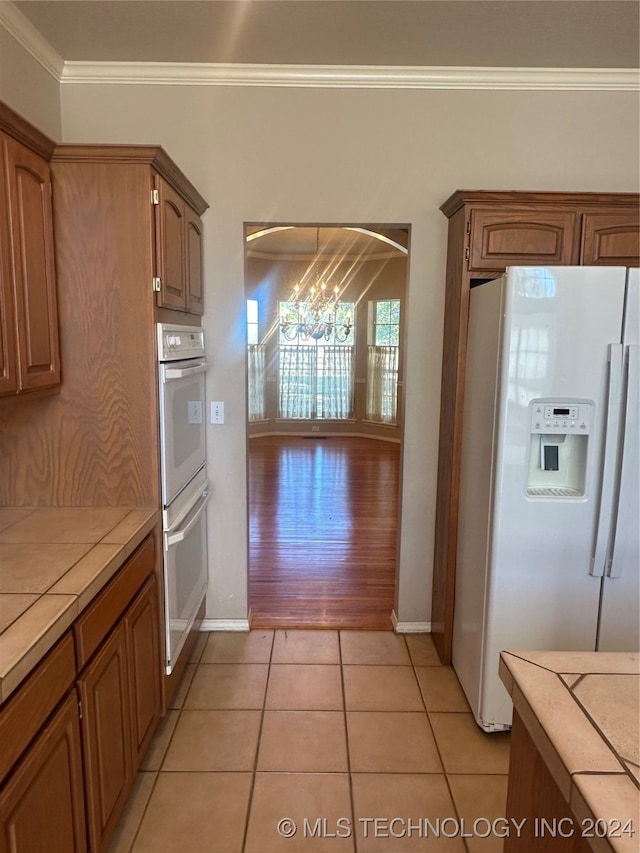 kitchen with white appliances, light hardwood / wood-style flooring, tile countertops, a notable chandelier, and crown molding