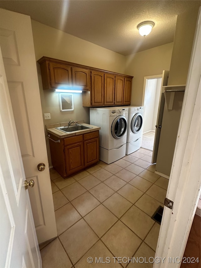 clothes washing area featuring light tile patterned flooring, cabinets, independent washer and dryer, sink, and a textured ceiling