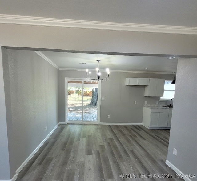 unfurnished dining area with a notable chandelier, sink, crown molding, and dark hardwood / wood-style flooring