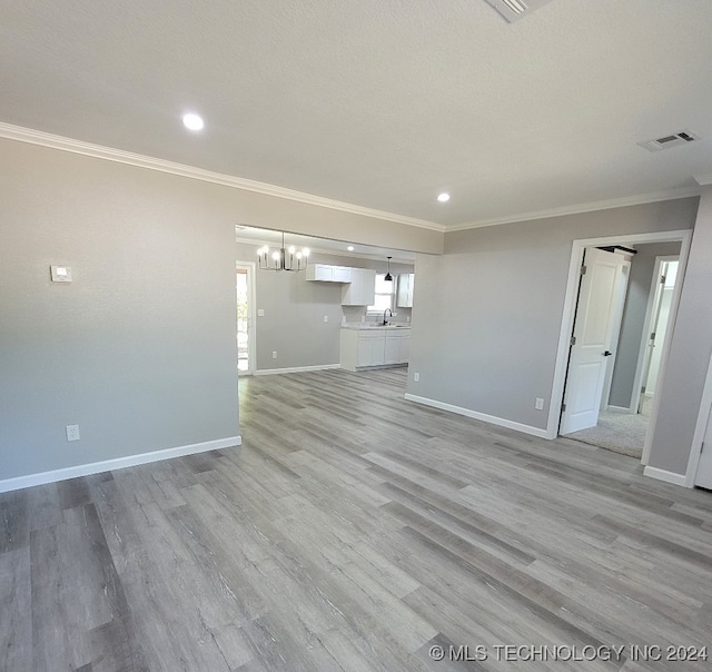 unfurnished living room featuring sink, light wood-type flooring, and ornamental molding