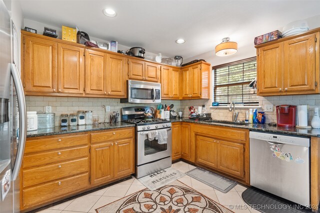 kitchen with dark stone countertops, stainless steel appliances, sink, and light tile patterned floors