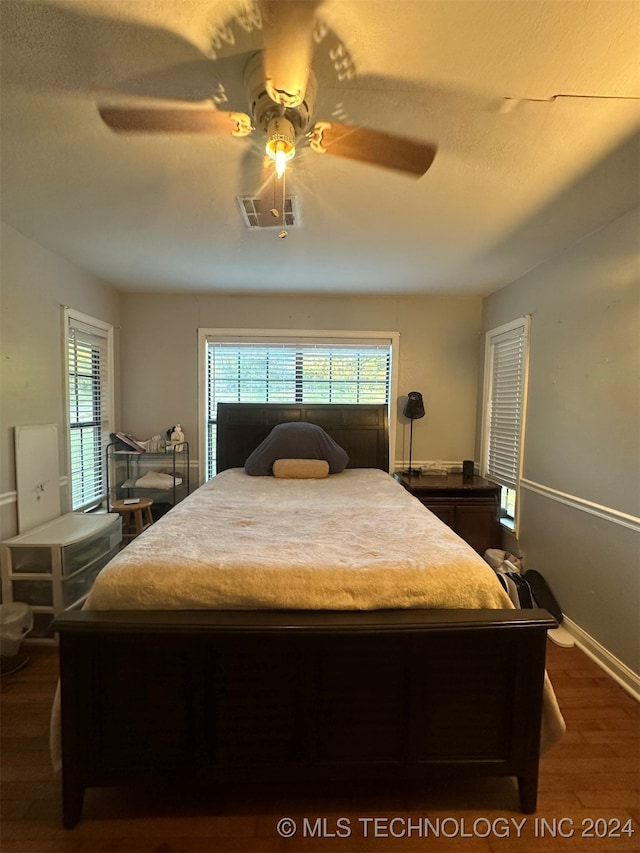 bedroom with a textured ceiling, ceiling fan, and dark wood-type flooring