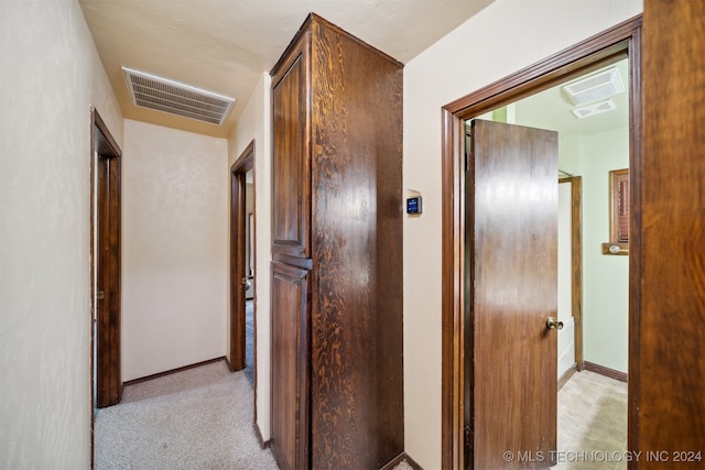 corridor with baseboards, visible vents, and light carpet