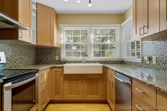 kitchen with sink, light wood-type flooring, stainless steel appliances, wall chimney exhaust hood, and light stone counters