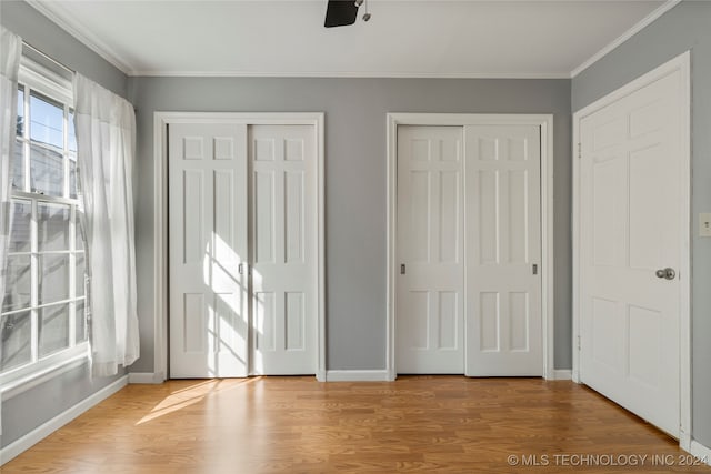 unfurnished bedroom with multiple closets, ornamental molding, light hardwood / wood-style floors, and ceiling fan