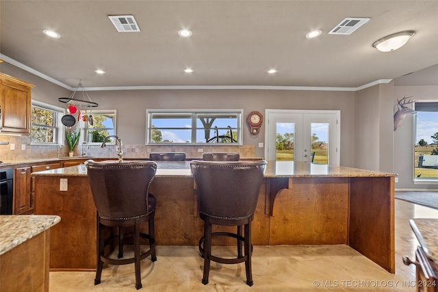 kitchen featuring a center island, light stone counters, ornamental molding, decorative backsplash, and french doors