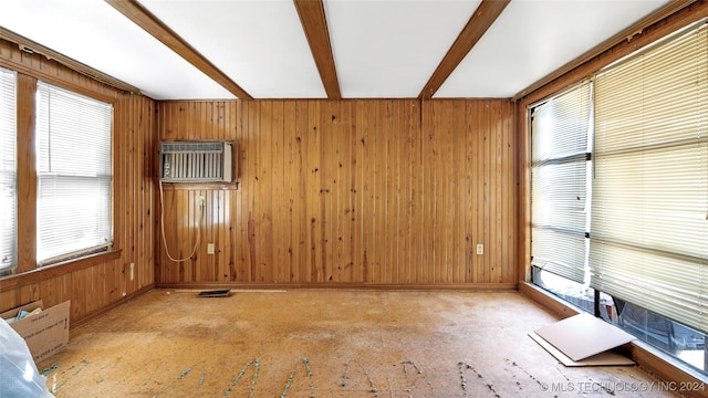 unfurnished living room with beam ceiling, wooden walls, a wall unit AC, and a wealth of natural light