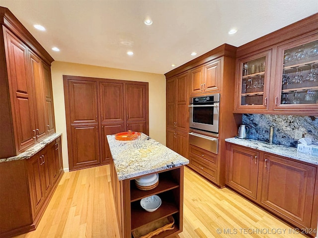 kitchen featuring oven, light hardwood / wood-style flooring, decorative backsplash, and light stone countertops