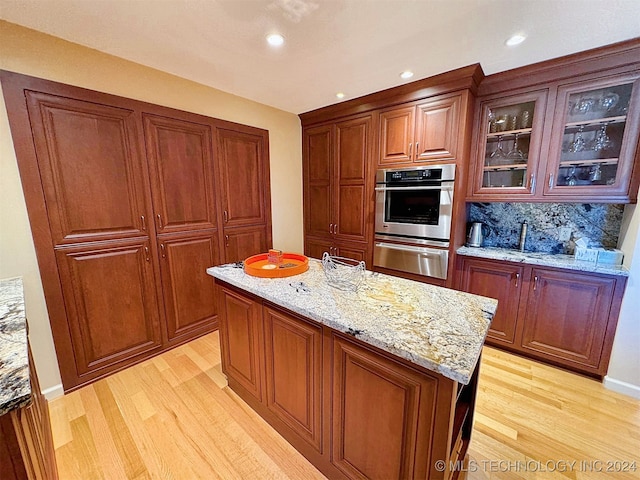 kitchen featuring a kitchen island, oven, backsplash, light stone countertops, and light hardwood / wood-style floors