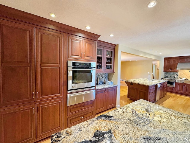 kitchen with backsplash, appliances with stainless steel finishes, light wood-type flooring, a center island, and light stone counters