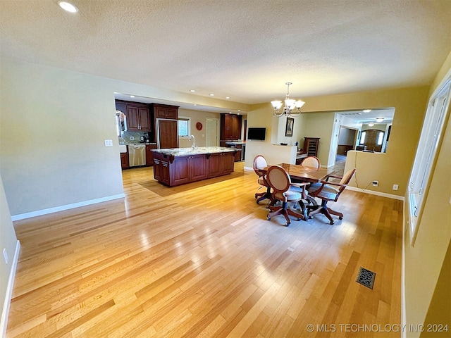 dining room with an inviting chandelier, a textured ceiling, and light wood-type flooring