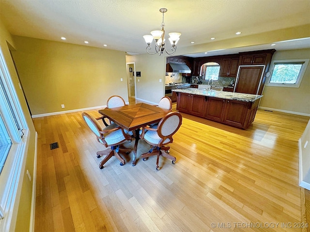 dining space with an inviting chandelier, sink, and light wood-type flooring