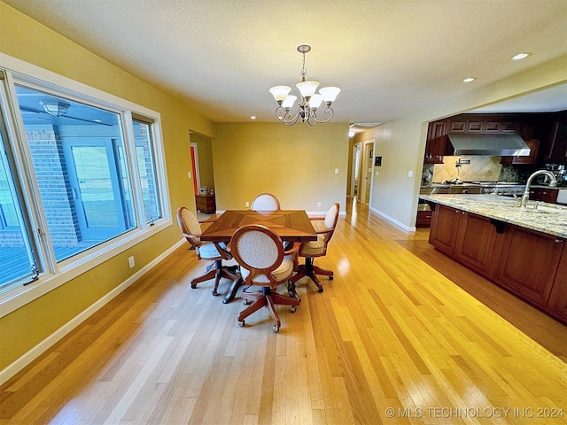 dining area featuring sink, a notable chandelier, a textured ceiling, and light hardwood / wood-style flooring