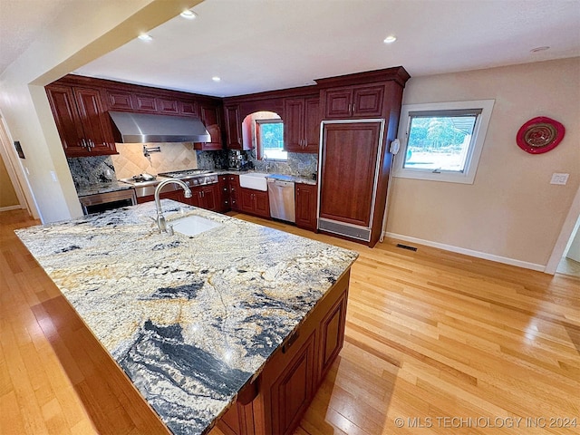 kitchen featuring sink, stainless steel appliances, light stone counters, decorative backsplash, and light hardwood / wood-style flooring